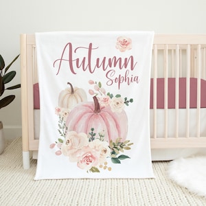 May include: White baby blanket with a pink and white watercolor pumpkin and floral design. The text "Autumn Sophia" is written in pink script.