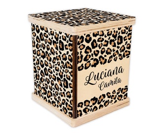 Op de afbeelding: Een houten doos met een luipaardprint. De doos heeft een deksel en is versierd met de namen "Luciana" en "Camila" in zwarte letters.