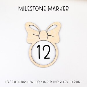 May include: Wooden milestone marker with a bow design and the number 12 in the center. The marker is made of 1/4 inch Baltic birch wood, sanded and ready to paint.