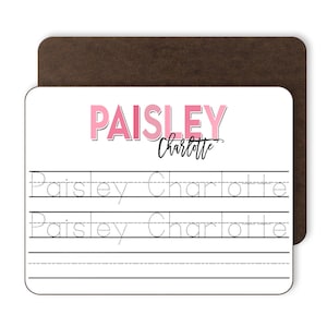 May include: A white dry-erase board with pink lettering that says "PAISLEY Charlotte". There are three lines with dotted lines for tracing the name "Paisley Charlotte".