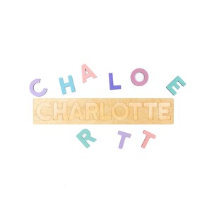 May include: Wooden name puzzle spelling "CHARLOTTE" in a natural wood color. Individual pastel-colored letters are scattered around the puzzle. The letters are in shades of pink, blue, purple, and green.