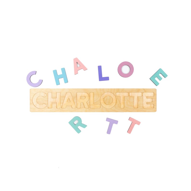 May include: Wooden name puzzle spelling "CHARLOTTE" in a natural wood color. Individual pastel-colored letters are scattered around the puzzle. The letters are in shades of pink, blue, purple, and green.