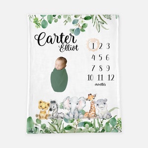 May include: A white baby blanket with a green leafy border. The blanket features a baby boy in a green swaddle, a lion, zebra, elephant, giraffe, and hippopotamus. The blanket also includes the text "Carter Elliot" and a number chart for tracking a baby's growth from 1 to 12 months.