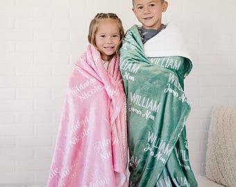 May include: Two children wrapped in personalized blankets. One child is wrapped in a pink blanket with the name "Adalyn Nicole" in white script. The other child is wrapped in a teal blanket with the name "William James Alan" in white script. The blankets are soft and plush.