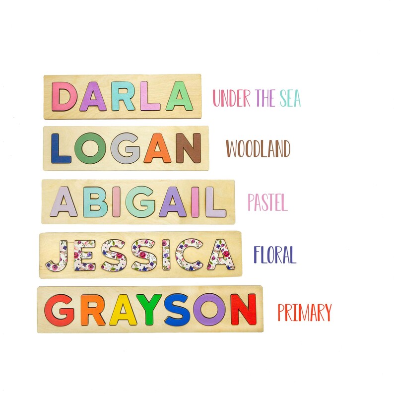May include: Wooden name puzzles with colorful letters. The names are DARLA, LOGAN, ABIGAIL, JESSICA, and GRAYSON. Each puzzle has a theme: Under the Sea, Woodland, Pastel, Floral, and Primary. The puzzles are on a white background.