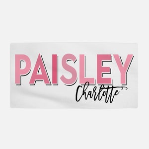 Op de afbeelding: Een witte handdoek met de naam "PAISLEY" in roze letters met een zwarte omtrek. De naam "Charlotte" staat eronder in cursief.