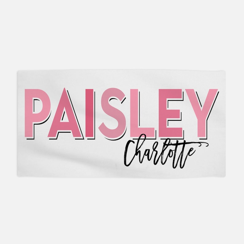 Op de afbeelding: Een witte handdoek met de naam "PAISLEY" in roze letters met een zwarte omtrek. De naam "Charlotte" staat eronder in cursief.