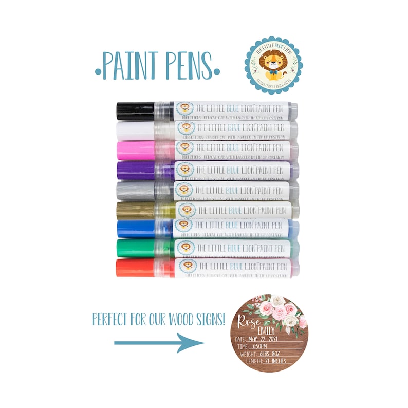 May include: A set of 10 paint pens with labels that say "The Little Blue Lion Paint Pen". The pens are arranged vertically in a row. Below the pens is a sign that says "Perfect for our wood signs!" and an arrow pointing to a round wooden sign with the text "Rose Emily" and birth details.