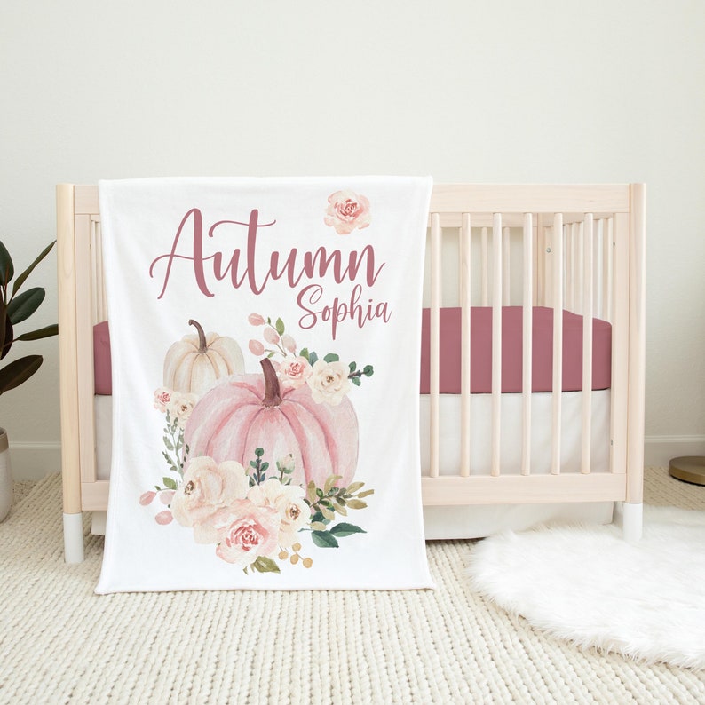 May include: White baby blanket with a pink and white watercolor pumpkin and floral design. The text "Autumn Sophia" is written in pink script.