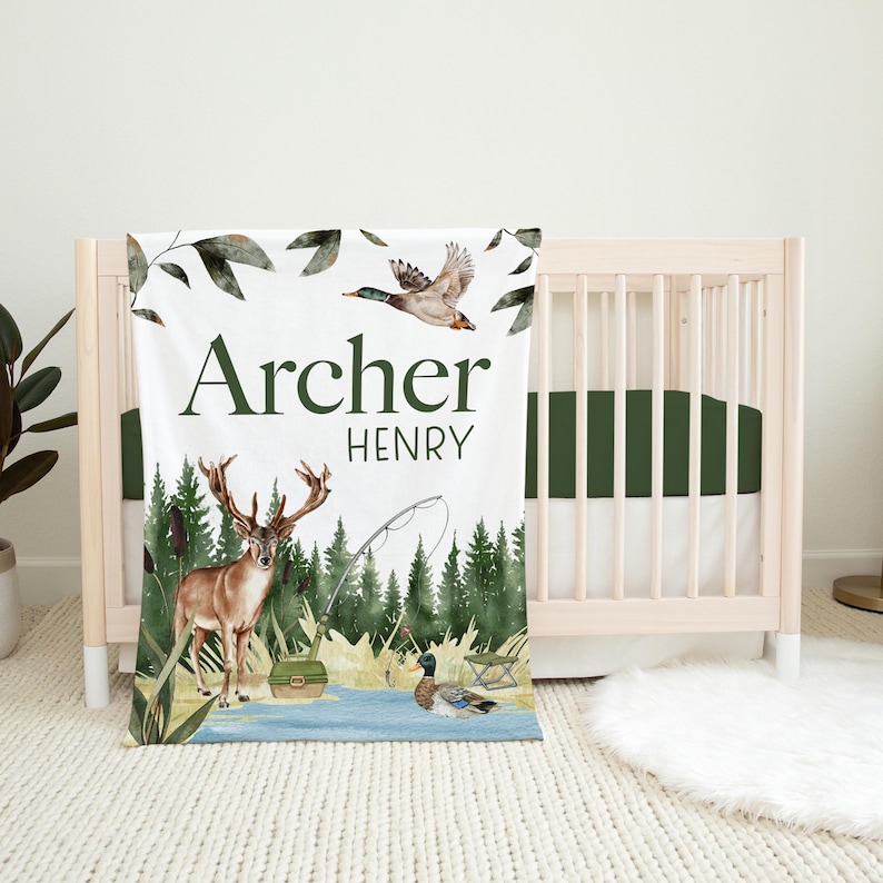 May include: A white baby blanket with a green forest scene featuring a deer, a fishing rod, and two ducks. The blanket has the name "Archer Henry" printed on it.