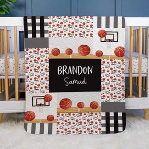 May include: A personalized baby blanket with a basketball theme. The blanket features a patchwork design with basketballs, hoops, and the name "Brandon Samuel" in white on a black background. The blanket is a mix of white, black, and gray.