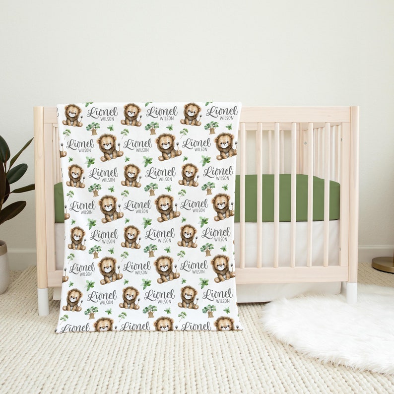 K&ouml;nnte beinhalten: Wei&szlig;e Babydecke mit einem sich wiederholenden Muster aus braunen L&ouml;wenjungen mit gr&uuml;nen Bl&auml;ttern und dem Namen "Lionel Wilson" auf jedem L&ouml;wenjungen.
