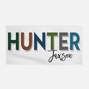 Op de afbeelding: Een witte handdoek met het woord "HUNTER" in kleurrijke letters, met de naam "Jaxson" eronder in cursief.