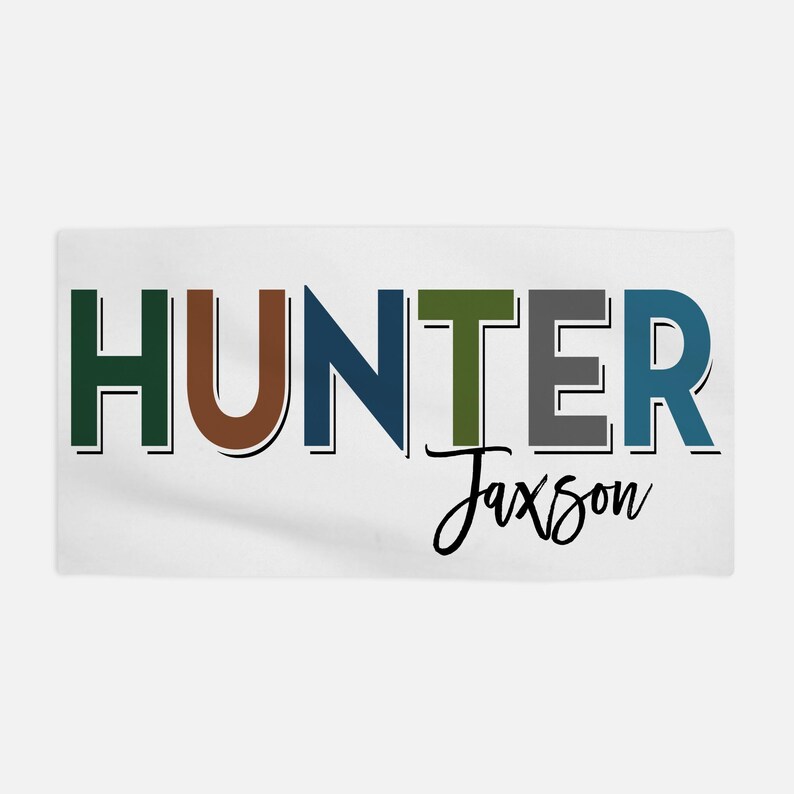 Op de afbeelding: Een witte handdoek met het woord "HUNTER" in kleurrijke letters, met de naam "Jaxson" eronder in cursief.