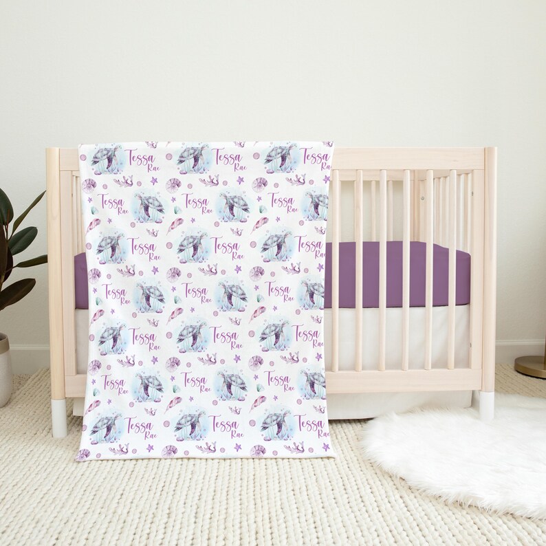 May include: A white baby blanket with a repeating pattern of purple watercolor sea turtles, seashells, and the name "Tessa Rae".