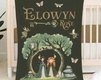 May include: A dark green baby blanket featuring a whimsical illustration. The blanket displays the name "ELOWYN Rose" in gold script, a key, fairies, butterflies, and two figures under a tree. The blanket is draped over a crib.