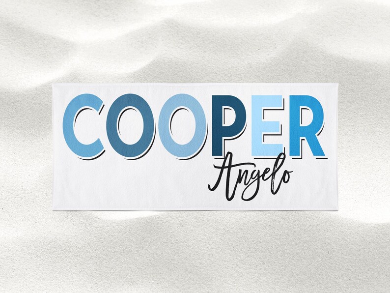 Op de afbeelding: Een witte strandhanddoek met de naam "COOPER" in blauwe letters met een blauw en wit ombre-effect. De naam "Angelo" staat eronder in cursief.