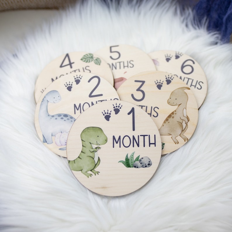 May include: Set of six wooden baby milestone cards featuring dinosaur illustrations. Each card has a number from 1 to 6 and the word "month" or "months".