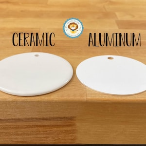 May include: Two white, round ceramic and aluminum ornaments with a hole at the top for hanging. The word "CERAMIC" is above the ceramic ornament, and "ALUMINUM" is above the aluminum ornament. The ornaments are on a wooden surface.
