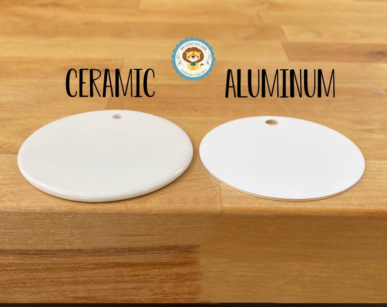 May include: Two white, round ceramic and aluminum ornaments with a hole at the top for hanging. The word "CERAMIC" is above the ceramic ornament, and "ALUMINUM" is above the aluminum ornament. The ornaments are on a wooden surface.