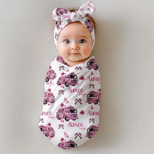 Pu&ograve; includere: Una copertina bianca per neonati con un motivo di camion dei pompieri rosa. La copertina riporta il nome "Aimee Leigh" ripetuto su tutto il motivo. Un cerchietto rosa con fiocco &egrave; sulla testa del bambino.