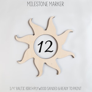 May include: A wooden sun-shaped milestone marker with a circle in the center that says "12". The marker is made of 1/4 inch Baltic birch plywood and is sanded and ready to paint.