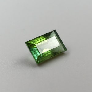 May include: A green gemstone with a rectangular cut. The gemstone is faceted and has a light green color.