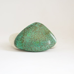 Può includere: Un cabochon di turchese verde con matrice marrone. La pietra ha una forma irregolare e una superficie liscia e lucida.