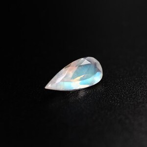 May include: A pear-shaped gemstone with a milky white colour and iridescent blue and green hues.