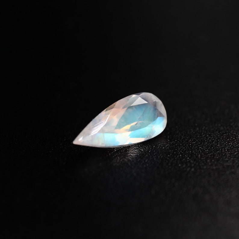 May include: A pear-shaped gemstone with a milky white colour and iridescent blue and green hues.