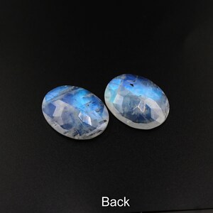 May include: Two oval-shaped moonstone cabochons with a blue iridescent sheen. The stones are faceted and have a smooth, polished finish.