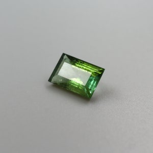 May include: A green and light green rectangular cut gemstone with facets.