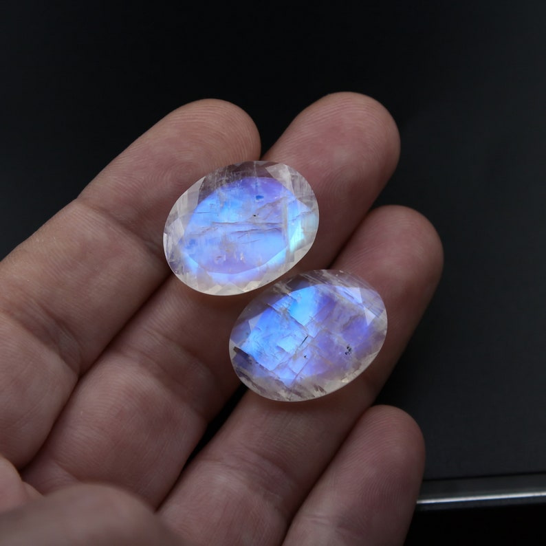 May include: Two oval-shaped moonstone cabochons with a iridescent blue sheen. The stones are translucent and have a white base.