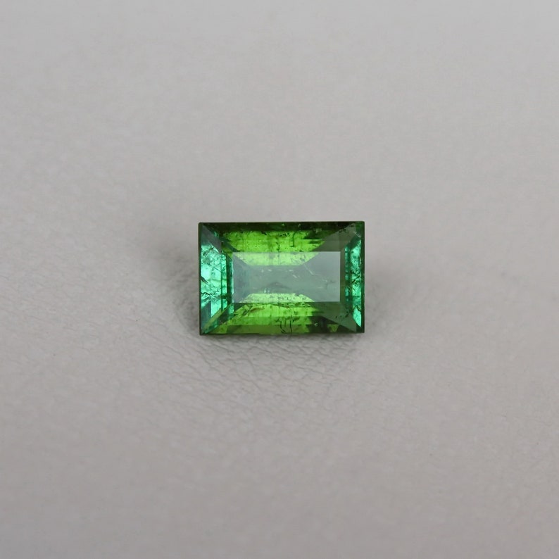 May include: A green gemstone with a rectangular cut and a faceted finish.