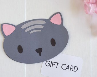 May include: A gray cat-shaped gift card holder with pink inner ears and a black nose and eyes. A white gift card with the words "GIFT CARD" is below the cat. The top of the image has the text "SVG • DXF • PNG • JPG".