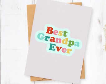 May include: A light purple greeting card with the words "Best Grandpa Ever" in colorful bubble letters. The card is on top of a brown envelope, set against a white wooden background.
