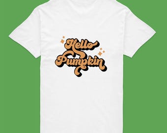May include: A white short-sleeved t-shirt featuring the text Hello Pumpkin in a stylized orange font with a black drop shadow. The design includes small orange four-pointed star accents positioned above and to the right of the lettering.