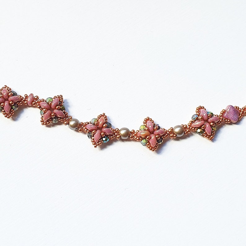 May include: A delicate pink and copper beaded necklace with a floral design. The necklace features small, intricate flower-shaped beads with a pink center and copper accents.