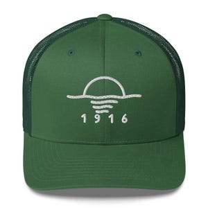 May include: A green trucker hat with a white embroidered design of a sun setting over water, and the number "1916" below. The hat has a mesh back and a curved brim.