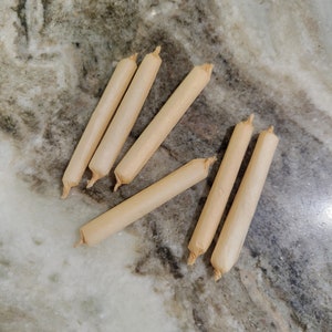 Op de afbeelding: Zes bruine papieren kegels, mogelijk voor het rollen van sigaretten, liggen op een lichtgrijs en bruin marmeren oppervlak.