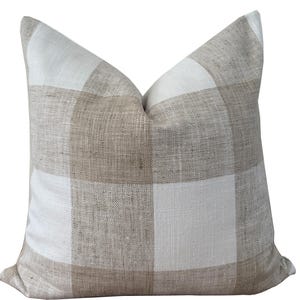 Könnte beinhalten: Quadratisches Zierkissen mit großem Büffelkaromuster in Beige und Weiß. Das Kissen hat eine strukturierte Optik und einen weichen, einladenden Look, perfekt, um jedem Raum einen Hauch von rustikalem Charme zu verleihen.