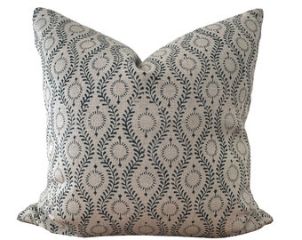 May include: A square decorative pillow with a beige background and a repeating pattern of dark blue stylized leaves and circular designs. The pillow has a soft, textured appearance and is likely made of fabric.