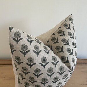 May include: A decorative pillow with a floral pattern. The pillow features a light beige background with a repeating pattern of dark gray flowers and leaves. The pillow is made of a soft fabric and is designed for home decor.