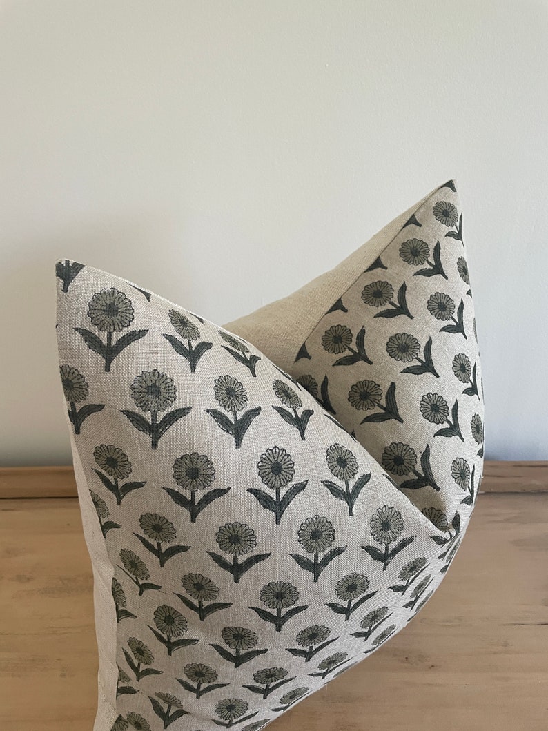 May include: A decorative pillow with a floral pattern. The pillow features a light beige background with a repeating pattern of dark gray flowers and leaves. The pillow is made of a soft fabric and is designed for home decor.