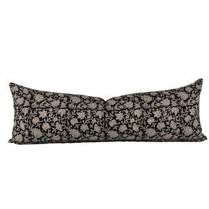 May include: A long, rectangular pillow with a black background and a cream-colored floral pattern. The pillow is designed for decorative use on a bed or sofa. The floral design is a repeating pattern of stylized flowers and leaves.
