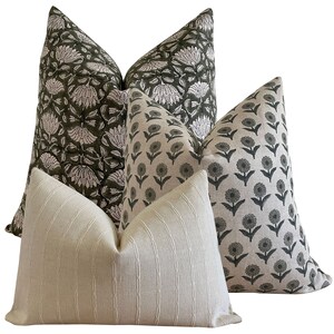 May include: Four decorative throw pillows with various patterns. Two pillows feature a dark green floral design on a white background. Another has a repeating floral pattern in dark green on a light background. The fourth pillow is a light cream color with vertical stripes.
