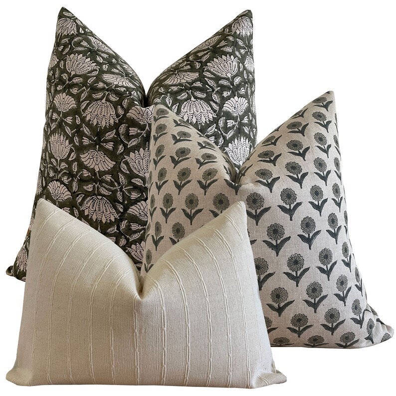 May include: Four decorative throw pillows with various patterns. Two pillows feature a dark green floral design on a white background. Another has a repeating floral pattern in dark green on a light background. The fourth pillow is a light cream color with vertical stripes.