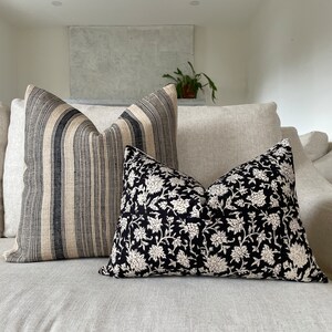 May include: Two decorative throw pillows on a light-colored sofa. One pillow features vertical black and beige stripes. The other pillow has a black background with a white floral pattern. The pillows add a decorative touch to the living room.