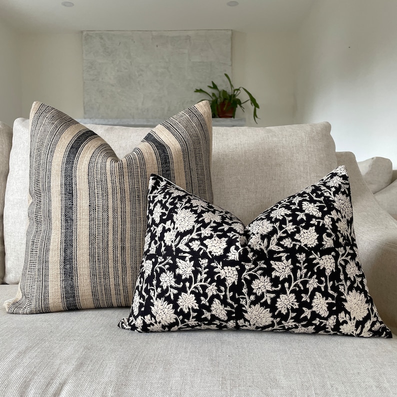 May include: Two decorative throw pillows on a light-colored sofa. One pillow features vertical black and beige stripes. The other pillow has a black background with a white floral pattern. The pillows add a decorative touch to the living room.