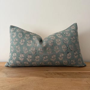 May include: A teal blue pillow with a white floral pattern. The pillow is made of a soft, comfortable fabric and has a subtle sheen.